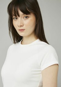 T-shirt blanc à manches courtes avec une texture lisse et un col rond, présentant des coutures d'épaule discrètes et une coupe ajustée.