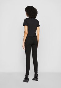 Camiseta negra ajustada combinada con jeans negros ajustados. El conjunto presenta una textura suave con mangas cortas, complementado con botas de tobillo de tacón.
