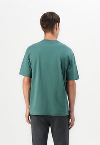 Grøn kortærmet t-shirt lavet af bomuld, med rund hals og en afslappet pasform. Ryggen er ensfarvet uden logoer eller mønstre.