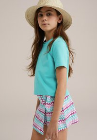 Turkio spalvos trumpomis rankovėmis marškiniai derinami su daugiaspalve zigzagų rašto sijonu, kuriame vyrauja rožinė, mėlyna ir balta spalvos. Pridėtas šiaudinis skrybėlė.