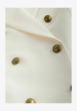 Sacou crem deschis cu o textură fină și design structurat. Prevăzut cu șase nasturi decorativi cu ton auriu.