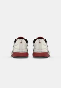 Hvite sportsko med svarte detaljer, en teksturert overdel og en rød og svart gummisåle. "NANO" er trykt på hælen.