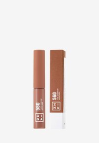Brow mascara in a brown tube with a matte finish and a cylindrical cap. Accompanied by a rectangular brown and white box featuring product text.
