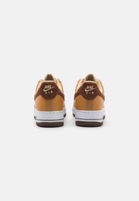 Nike Air tornacipő barna velúr díszítéssel, narancssárga bőr felsőrésszel, fehér középtalppal és sötétbarna talppal. A sarokon logóval ellátva.
