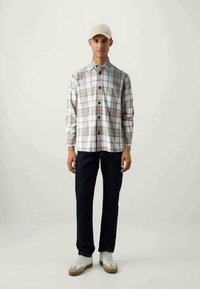 Chemise à carreaux blanche, marron et beige ; associée à un pantalon sombre et des baskets blanches. Caractéristiques : manches longues et coupe décontractée.