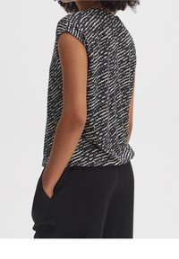 Black and white patterned short-sleeve top with a loose fit, featuring a round neckline and soft fabric, paired with black trousers.