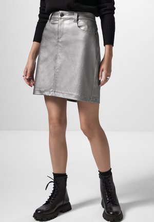 Jupe A-line en argent métallique avec poches avant, passants de ceinture et fermeture éclair, associée à des bottes de combat noires à lacets.