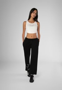 White cropped tank top with rhinestone detail and black sweatpants featuring embroidery at the hem. Black athletic shoes complete the look.
