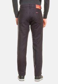 Jeans scuri con una vestibilità a gamba dritta, realizzati in un tessuto resistente. Presentano un'etichetta rossa in vita e due tasche posteriori.