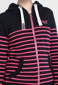 Felpa con cappuccio a zip, a righe nere e rosa, dotata di zip argentata, tasche frontali e logo del marchio sul petto.