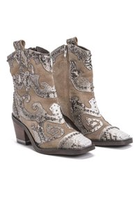 Botas de vaquero de ante en tono marrón con adornos plateados, paneles texturizados y puntas blancas en forma de flecha. Cuentan con un bajo tacón apilado y cremallera.