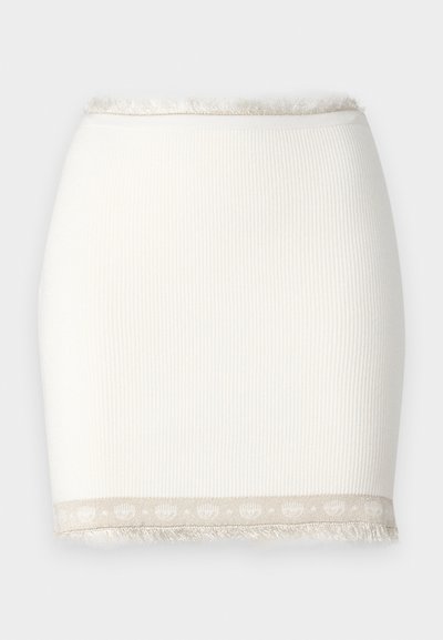 Hvit ribbestrikket skjørt med en tettsittende fasong og frynse detaljer i kanten. Har en lys beige aksent med et mønster. Jevn tekstur.