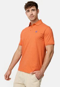 Polo orange en tissu texturé, avec une patte de boutonnage à trois boutons et un petit logo bleu sur la poitrine. Manches courtes et design ajusté.