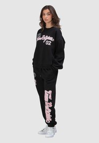 Sweat-shirt noir et jogging en coton, avec un logo rose et des accents assortis. Le sweat-shirt présente un col ras du cou et une coupe décontractée.