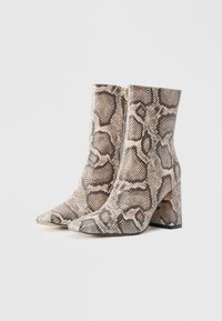 Bottes hauteur cheville avec orteils pointus et talons blocs, présentant un motif en peau de serpent beige et noir et des zips latéraux.
