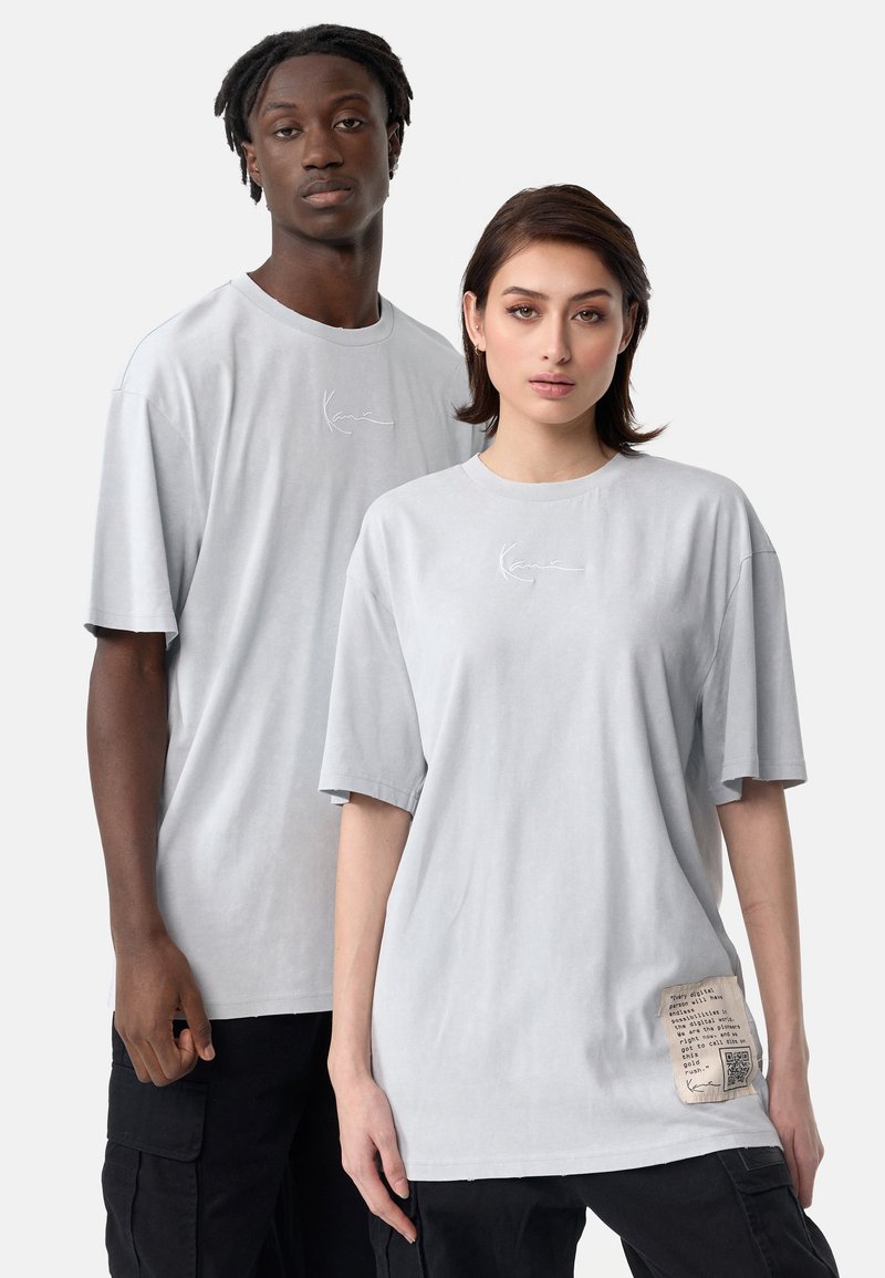 Šviesiai pilkos, per didelius t-shirt marškiniai iš medvilnės mišinio, turintys trumpas rankoves ir šoninės etiketės su spausdintu tekstu bei QR kodu.