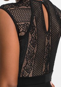 Černé šaty s jemnými krajkovými a síťovinovými panely, s detailem klíčové díry na zádech a přiléhavým pasem. Textura je jemná a vrstvená.