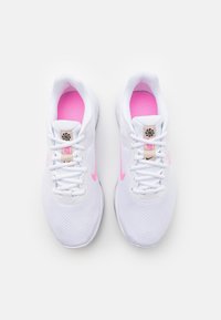 Bílé sportovní boty s růžovými akcenty, síťovinový svršek, kulatá špička a bílé šněrování. Obsahují štítek s logem poblíž jazyka a texturovanou podrážku.
