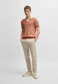 Kortärmad, rostfärgad stickad polo med krämfärgad krage och manschetter, åtföljd av ljusbeige byxor och krämfärgade sneakers.