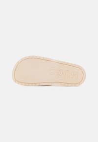 Gummisåle i lys beige med rillemønster, som har det pregete merkenavnet "HUGO" og et glatt, rundt kantdesign.