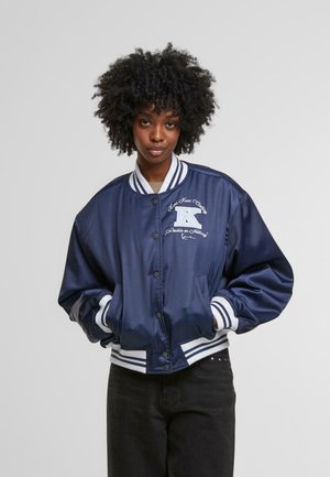 Veste bomber en satin marine avec des poignets et un ourlet côtelés rayés blancs. Présente un logo sur la poitrine gauche et une coupe décontractée et surdimensionnée.