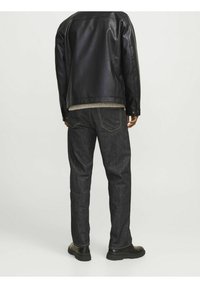 Svart läderjacka över en grå tröja, matchat med mörka denimjeans. Jeansarna har gula sömmar och rak benform. Svarta skor.