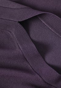 Prim-plan cu țesătură tricotată în nuanță mov închis, pliata, cu dungi și cusături detaliate, textura fiind vizibilă.