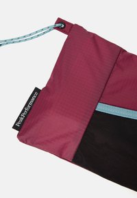Pochette rouge et noire en tissu texturé, avec un cordon de serrage bleu et une étiquette Peak Performance. Fermeture éclair en haut et design élégant.