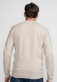 Lichtbeige trui met horizontale ribbeltextuur, ronde hals, lange mouwen en aansluitende manchetten. Minimalistisch ontwerp, geschikt voor lagen.