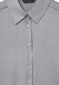 Blusa satin grigia con colletto classico, caratterizzata da una chiusura frontale con bottoni e una texture liscia. I bottoni sono circolari e abbinati al colore del tessuto.