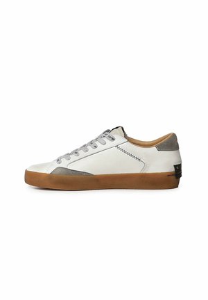 Sneaker bassa bianca con dettagli in suede grigio, lacci grigi e suola in gomma marrone su sfondo bianco.