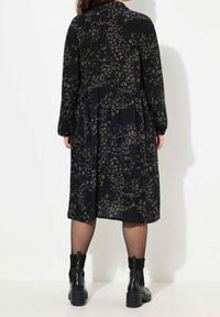 Abito nero con un sottile motivo a stampa animale, maniche lunghe, schiena plissettata e una vestibilità rilassata. Abbinato a stivaletti neri chunky.