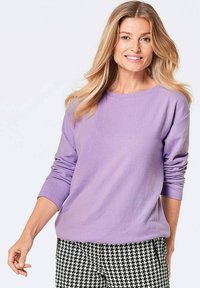 Lila Pullover mit langen Ärmeln, rundem Ausschnitt, weichem Textil, kombiniert mit gestreiften Schwarz-Weiß-Hahnentritthosen.