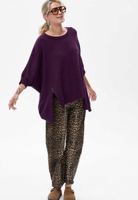 Fioletowy, oversize sweter z okrągłym dekoltem i bocznymi rozporkami, w połączeniu z luźnymi spodniami w panterkę. Brązowe buty wsuwane.