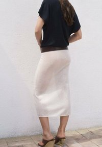 Czarny top z krótkim rękawem w połączeniu z dopasowaną, kremową spódnicą midi. Spódnica ma subtelną fakturę i gładkie wykończenie. Brązowe sandały na koturnie.