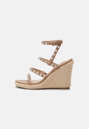 Beige kilehæle sandaler med flettet jutesål, tre smalle stropper dekoreret med sølvnitter og en ankelrem med spænde.