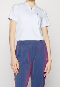 Haut bleu clair à manches courtes avec col mandarin et fermeture éclair, associé à un pantalon rayé bleu et rose doté d'une taille élastique.