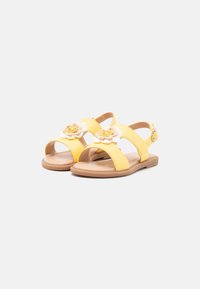 Sandalias amarillas con dos correas, acentos florales y una suela plana. Hechas de material sintético suave con una plantilla color tostado. Hebilla ajustable.