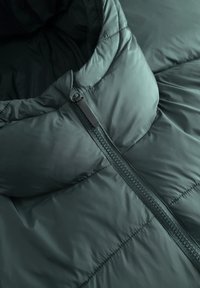 Veste matelassée vert foncé avec un col relevé et un zip central partiellement remonté.