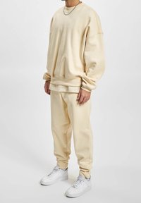 Felpa beige oversize con polsini e orlo a coste, abbinata a pantaloni tapered coordinati; indossata con sneakers bianche. Texture in morbido cotone misto.