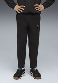 Zwarte sportbroek met een taps toelopende pasvorm en zijzakken, met een klein grijs Puma-logo op de linkerdij. Draag ik met zwarte sneakers.