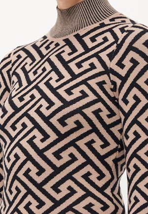 Pull à col roulé beige et noir à motif géométrique avec col côtelé, porté sur le haut du torse.