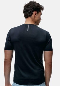 Melna sporta T-kreklu ar īsām piedurknēm, gluda tekstūra un vertikālā atstarojošā josla aizmugurē. Pieguļošs dizains, minimālisma stils.