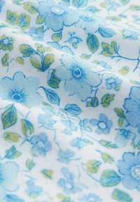 Tela suave con un estampado floral azul y verde, con flores y hojas detalladas sobre un fondo blanco.