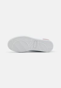 White rubber sneaker sole with zigzag pattern and branded label. Smooth texture, rounded shape, and minimalistic design.