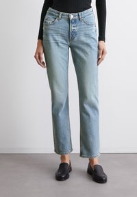 Vaqueros de pierna recta en azul claro con cintura alta, diseño de cinco bolsillos, lavado frontal y detalles de costura sutiles. Combinados con mocasines negros.