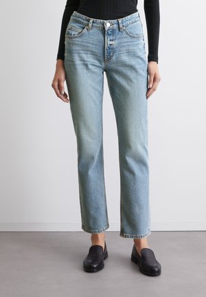 Vaqueros de pierna recta en azul claro con cintura alta, diseño de cinco bolsillos, lavado frontal y detalles de costura sutiles. Combinados con mocasines negros.