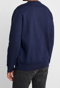 Tmavě modrá mikina s kulatým výstřihem, žebrovanými manžetami a lemem. Vyrobena z měkkého materiálu s hladkým povrchem, bez viditelného značení.