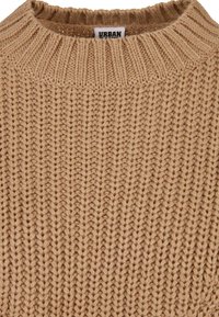 Pull beige en maille épaisse avec col rond côtelé et grosses coutures verticales texturées, avec une étiquette de marque "URBAN" à l'intérieur du col.
