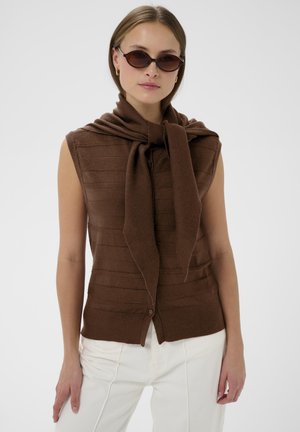 Brown knitted sleeveless sweater with a tied scarf at the neck. Features horizontal striped texture and button closure, paired with white pants.
